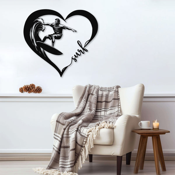 Black metal wall art featuring a surfer riding a wave inside a heart shape with the word 'surf' written in cursive. The art is displayed on a light gray wall above a cozy armchair with a plaid blanket draped over it.