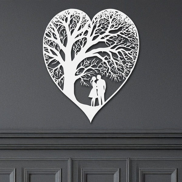 A white heart-shaped metal wall decor with a detailed tree-like pattern with a couple, representing the theme of everlasting love on a grey wall.