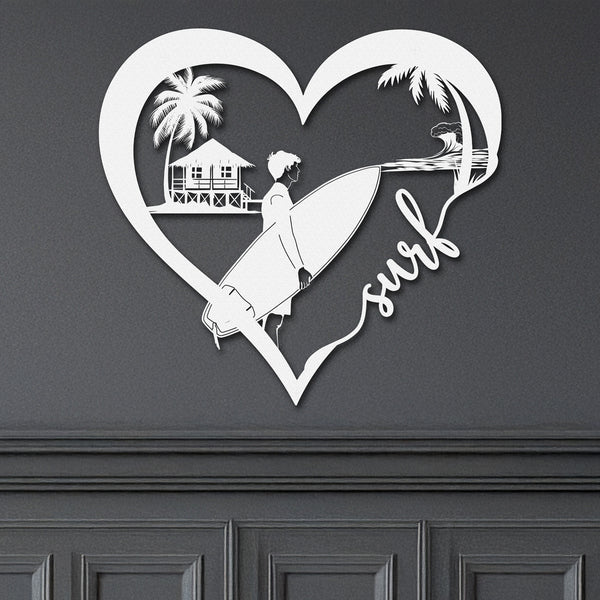 White metal wall art featuring a surfer looking at riding a wave inside a heart shape with the word 'surf' written in cursive. The art is displayed on a dark wall above wainscoting.