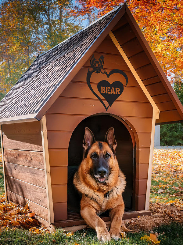 A German Shepherd dog sitting in a wooden doghouse with a custom metal sign above the entrance featuring a heart shape and the name 'BEAR'