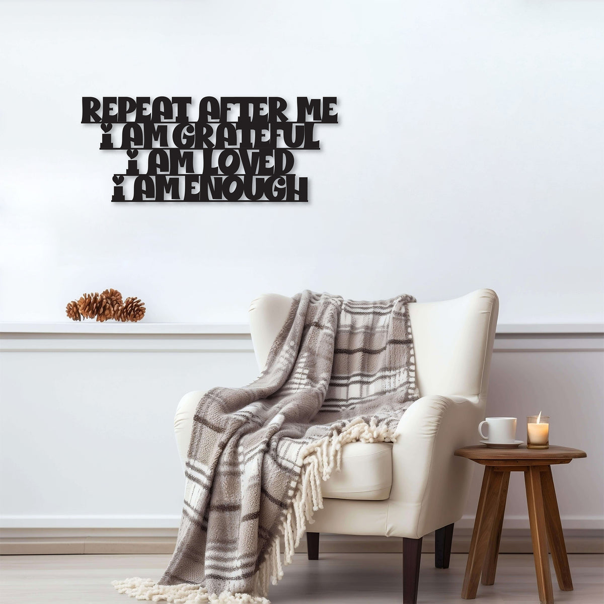 Black metal die-cut sign with the phrase 'Repeat After Me I Am Grateful I Am Loved I Am Enough' displayed above a cozy armchair with a plaid blanket.