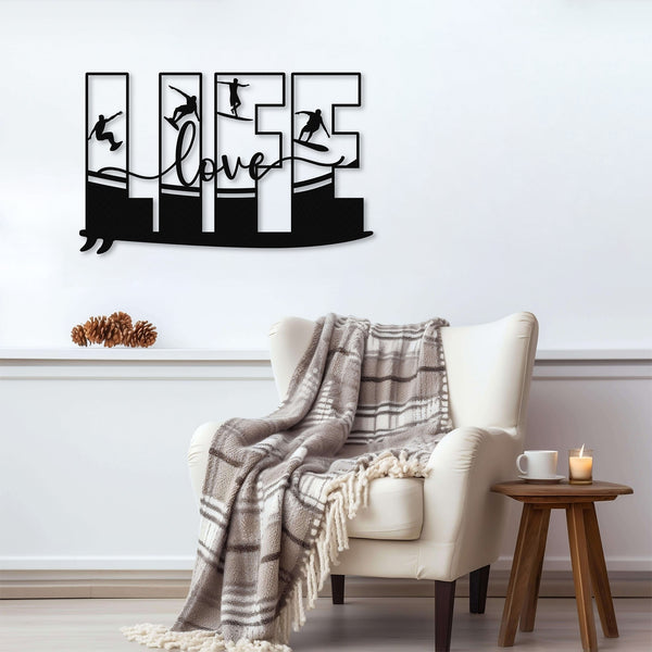 Black metal wall art featuring the word 'LIFE' with silhouettes of surfers in various poses within each letter, mounted above an armchair with a plaid blanket.
