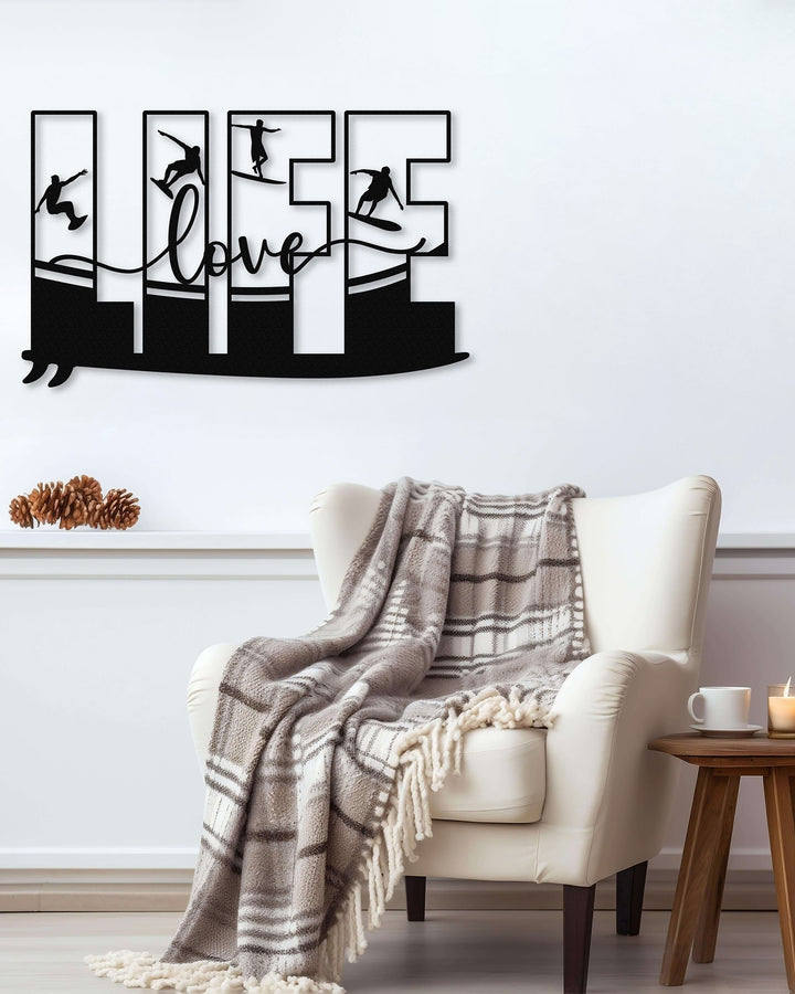 Black metal wall art featuring the word 'LIFE' with silhouettes of surfers in various poses within each letter, mounted above an armchair with a plaid blanket.