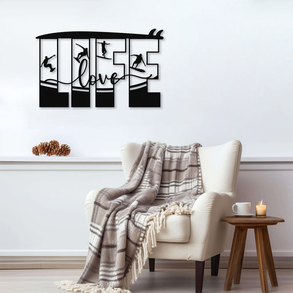 Black metal wall art featuring the word 'LIFE' with silhouettes of surfers in various poses within each letter, mounted above an armchair with a plaid blanket.