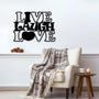 Black metal wall decor with the phrase 'Live Laugh Love' displayed above an armchair with a plaid blanket.