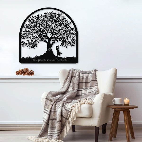 A black and white metal heart-shaped wall decor with a detailed tree-like pattern and two silhouettes of a couple embracing, representing the symbol of everlasting love. At the bottom in cursive it says 