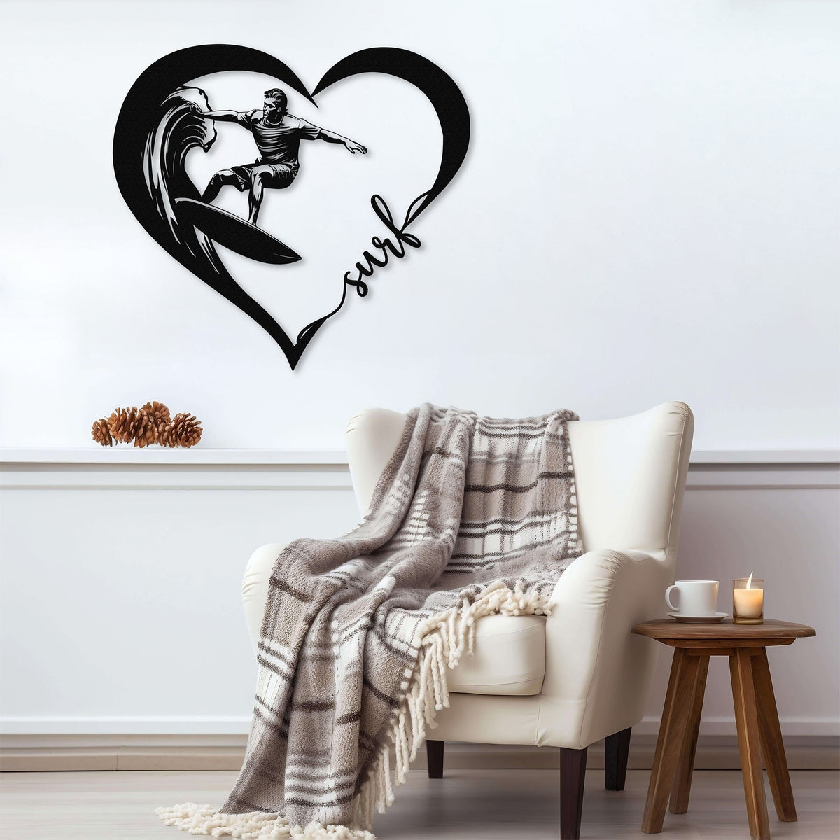 Black metal wall art featuring a surfer riding a wave inside a heart shape with the word 'surf' written in cursive. The art is displayed on a light gray wall above a cozy armchair with a plaid blanket draped over it.