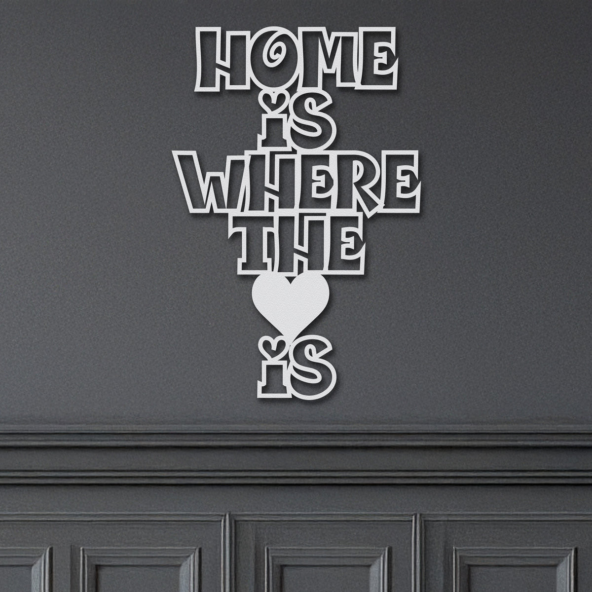 Close-up of a white metal sign with the phrase 'Home Is Where The Heart Is' and a small heart icon.