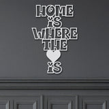 Close-up of a white metal sign with the phrase 'Home Is Where The Heart Is' and a small heart icon.