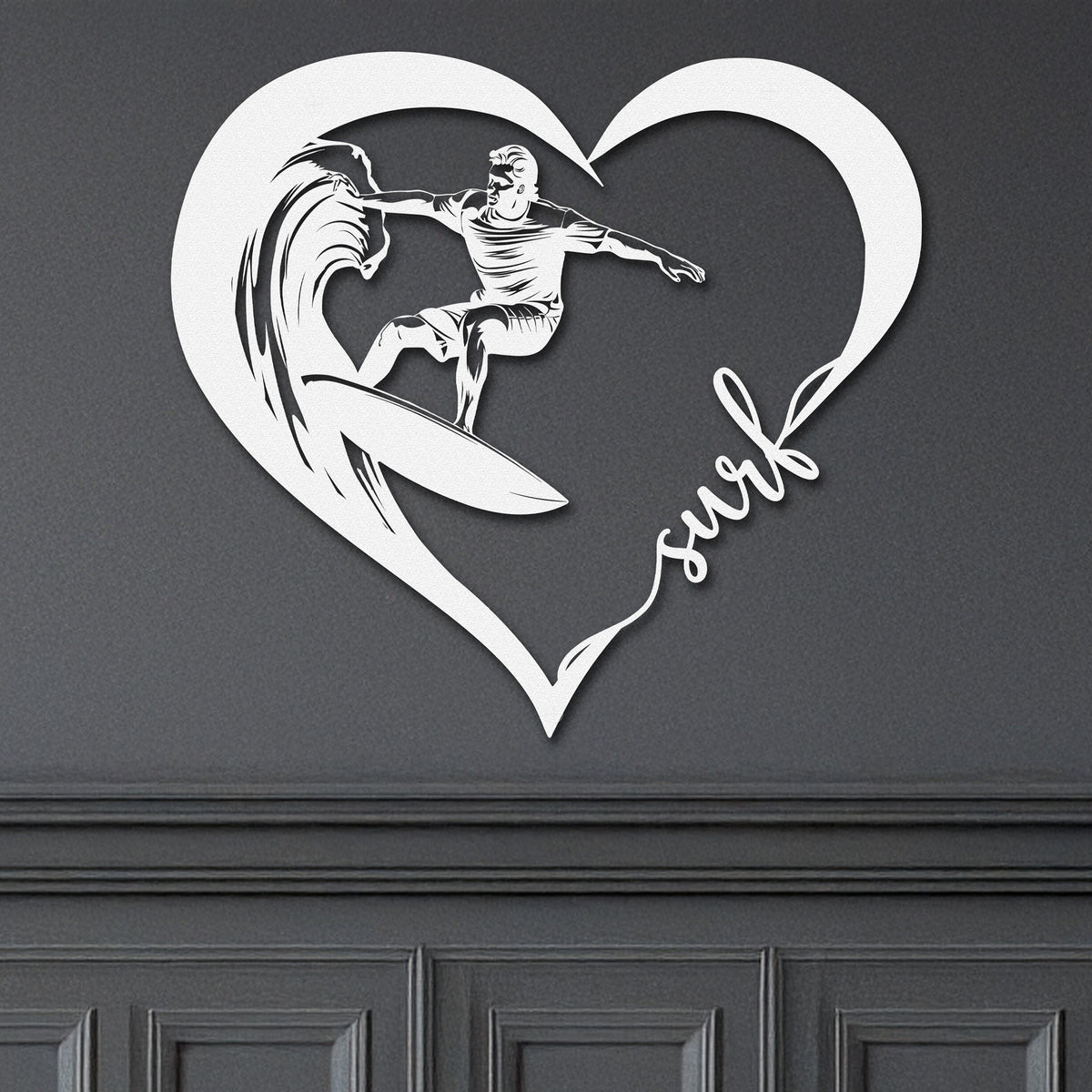 White metal wall art featuring a surfer riding a wave inside a heart shape with the word 'surf' written in cursive. The art is displayed on a dark grey wall.