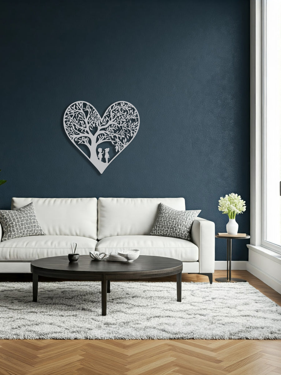 White metal heart wall art featuring two children playing beneath a tree, displayed above a white sofa in a living room with large windows.
