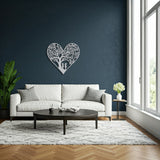 White metal heart wall art featuring two children playing beneath a tree, displayed above a white sofa in a living room with large windows.