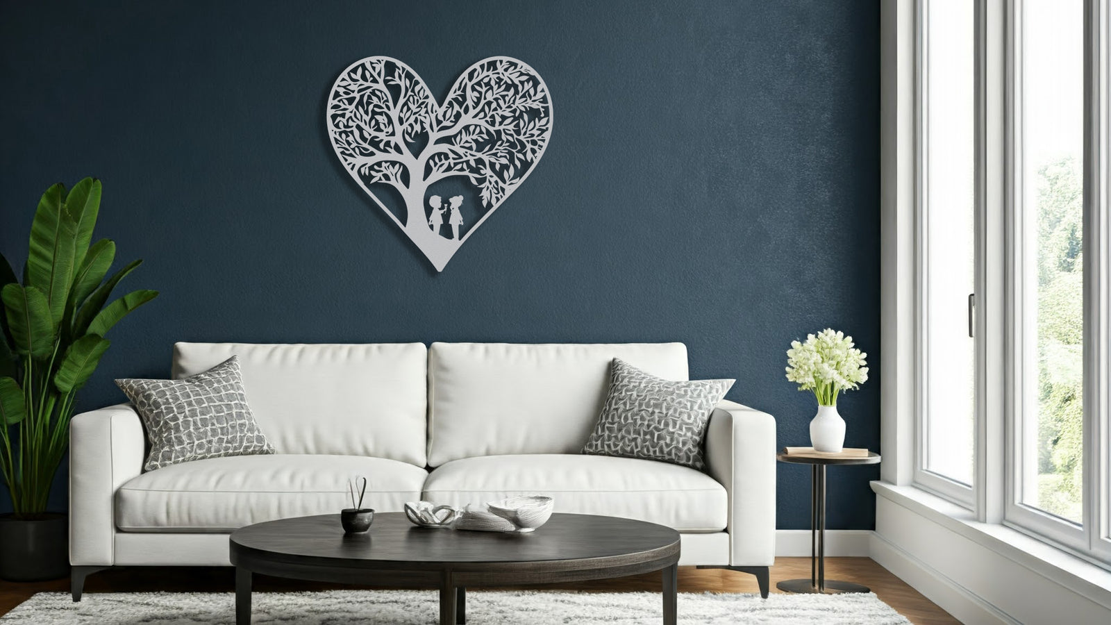 White metal heart wall art featuring two children playing beneath a tree, displayed above a white sofa in a living room with large windows.