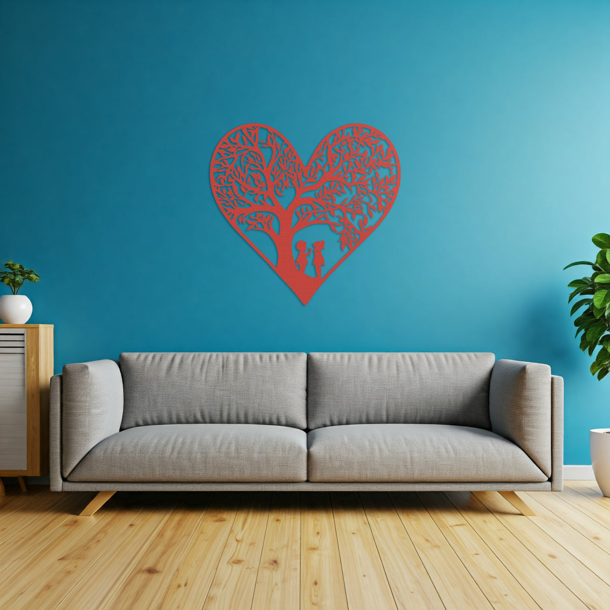 Red metal heart wall art featuring two children playing beneath a tree, displayed above a gray sofa in a living room.