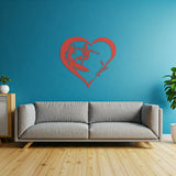 Red metal wall art featuring a surfer riding a wave inside a heart shape with the word 'surf' written in cursive. The art is displayed on a light blue wall above a gray sofa in a living room setting.