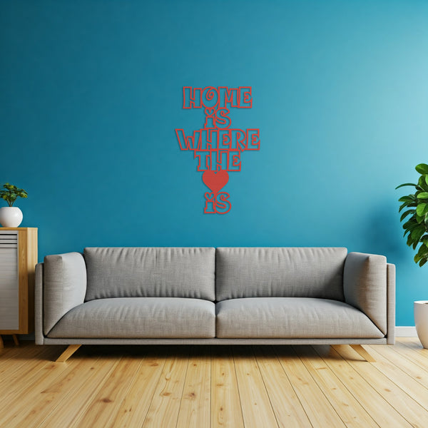Red metal sign with the phrase 'Home Is Where The Heart Is' displayed above a gray sofa in a living room.