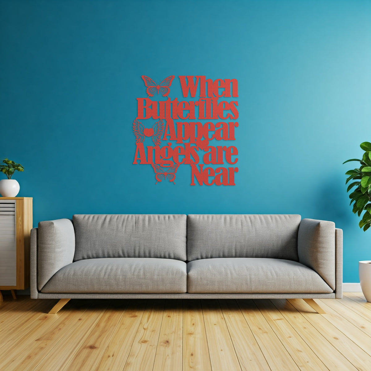 Red metal wall decor with a cutout butterfly and the quote "When Butterflies Appear, Angels are Near" hanging above a gray couch in a living room