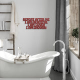 Red metal inspirational sign hanging next to a white bath tub, the sign says 