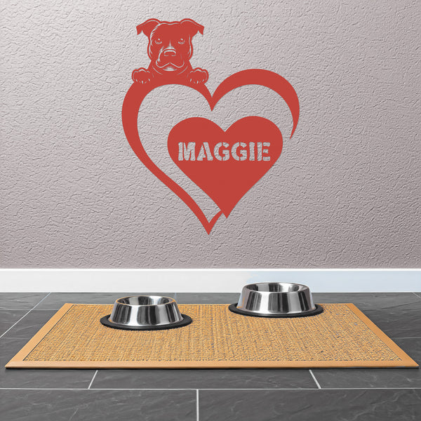 Red metal sign featuring a pit bull and a heart-shaped name plaque, displayed on a light-colored wall above 2 dog bowls.