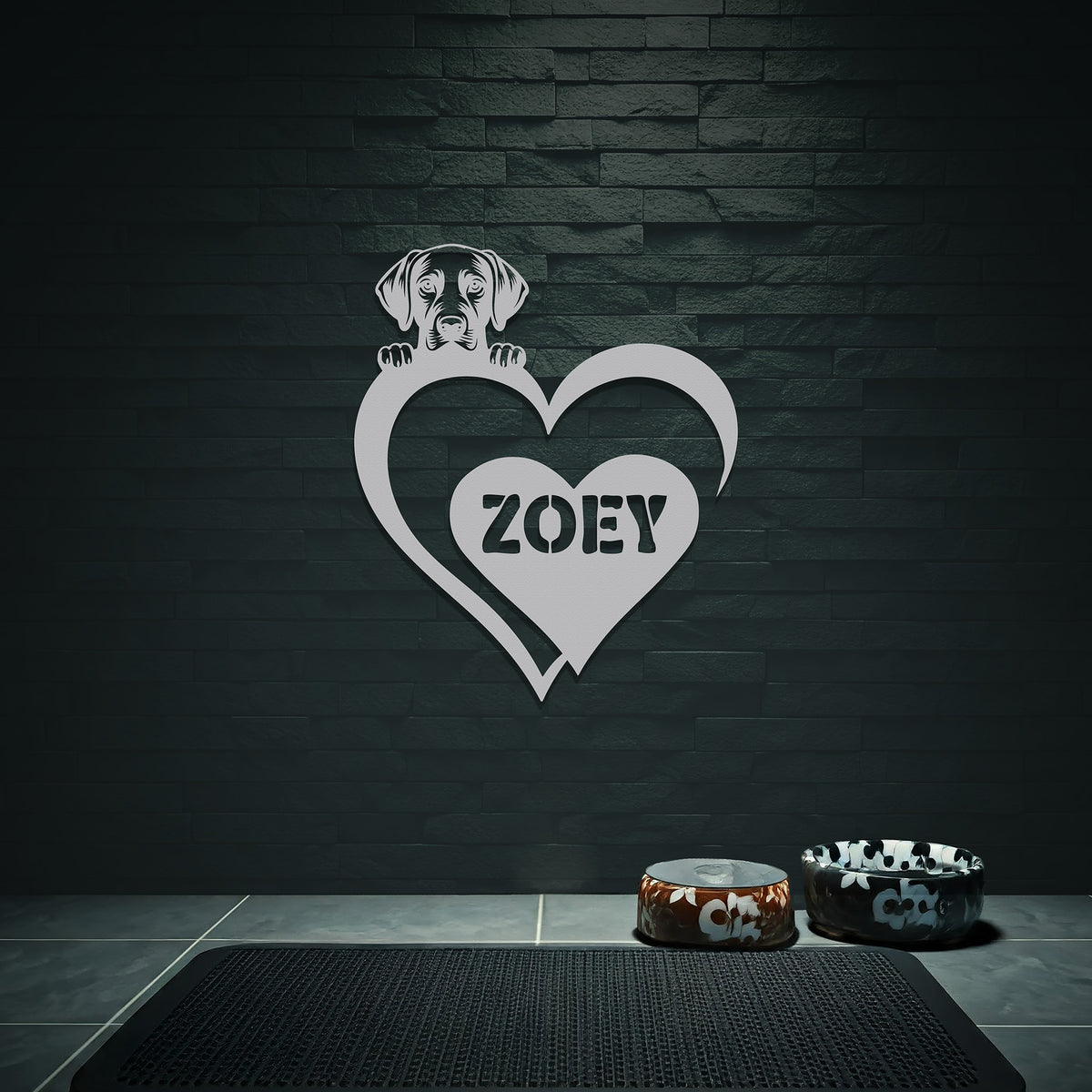 White metal sign with a dog silhouette peeking over a heart, with the name "Zoey" written inside the heart, hanging on a grey wall above dog bowls.