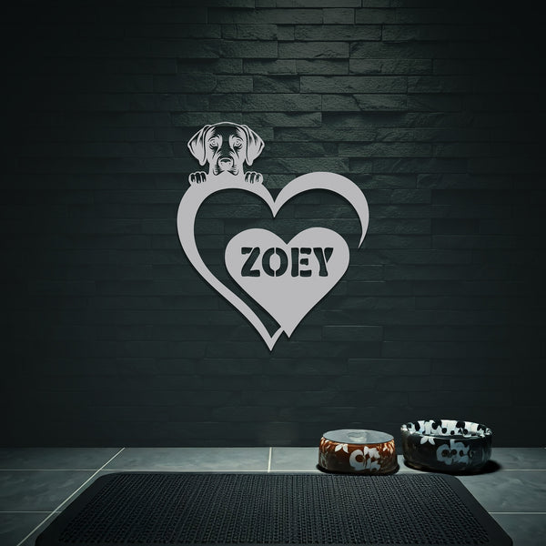 White metal sign with a dog silhouette peeking over a heart, with the name "Zoey" written inside the heart, hanging on a grey wall above dog bowls.